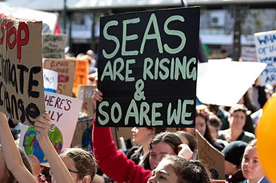 A sign at a school strike for climate in Dunedin reads, 'Seas are rising & so are we'.